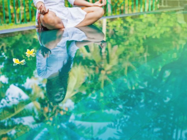 Person meditating by a reflective pool with floating flowers.
