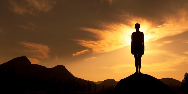 Silhouette of person standing on rock at sunset.