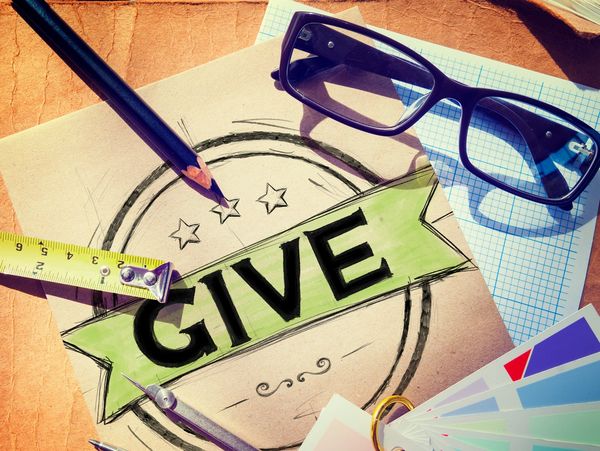 Desk with art supplies surrounding a drawing of the word GIVE on paper.