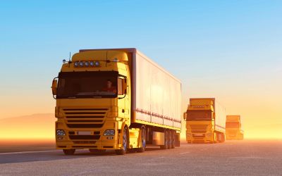 Three yellow trucks driving on a road at sunset.