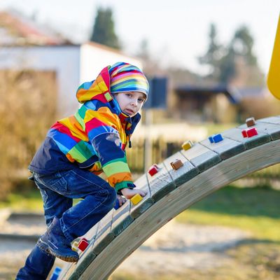 Child in colorful jacket climbing playground equipment outdoors.