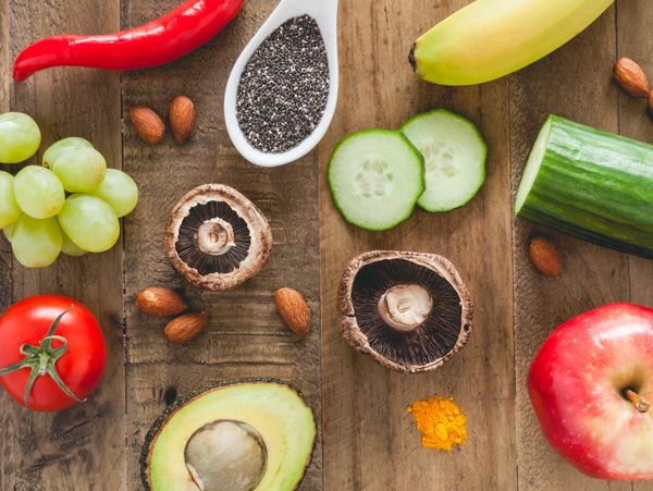 Assortment of fresh fruits, vegetables, nuts, and seeds on a wooden surface.