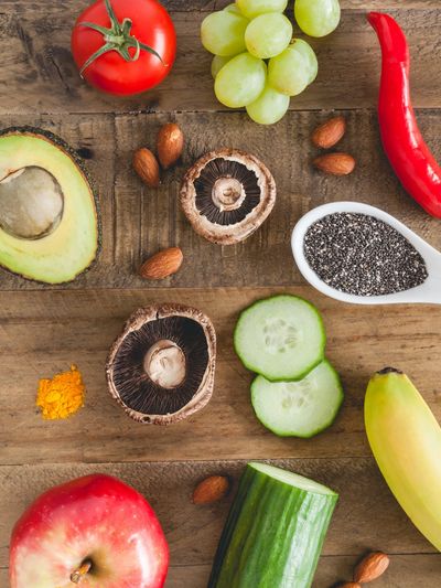 Various fresh fruits, vegetables, nuts, and seeds arranged on a wooden surface.