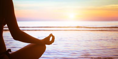 Person meditating by the ocean at sunset.