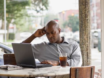 Man working on laptop at a cafe with a drink.