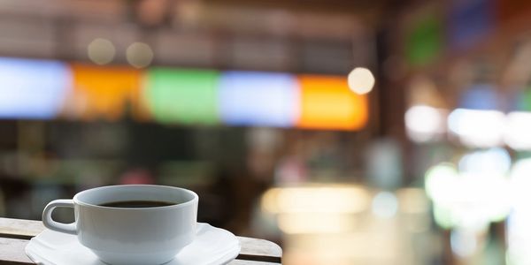 A cup of coffee on a table in a cozy cafe with colorful lights in the background.
