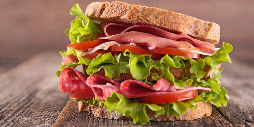 A fresh sandwich with lettuce, tomato, and various deli meats on whole grain bread.
