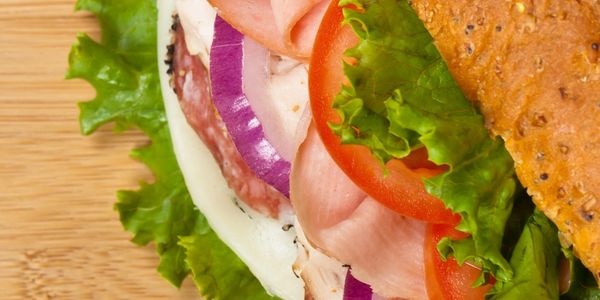Close-up of a fresh sandwich with lettuce, tomato, onion, and deli meats.