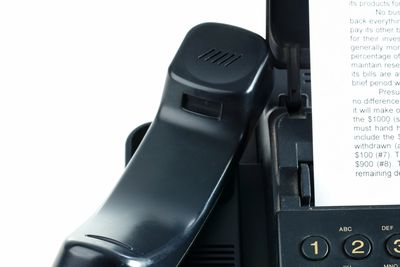 Close-up of a black telephone handset on a fax machine with a document inserted.