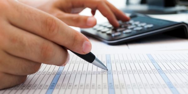 A person using a calculator to perform calculations, with a pen in hand, writing down the results on a piece of paper