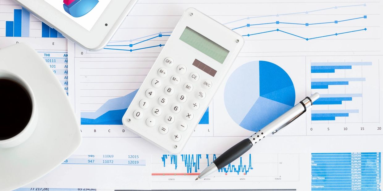 Calculator, pen, and coffee on financial charts and graphs.