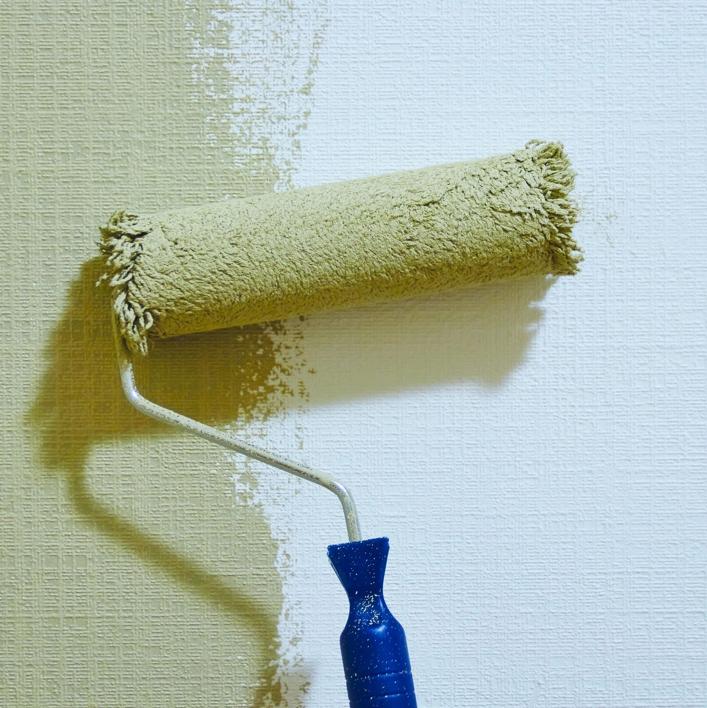 Paint roller against a wall that is partially painted.