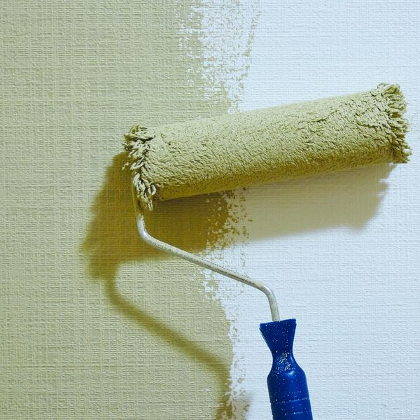 Paint roller applying light green paint on a textured wall.