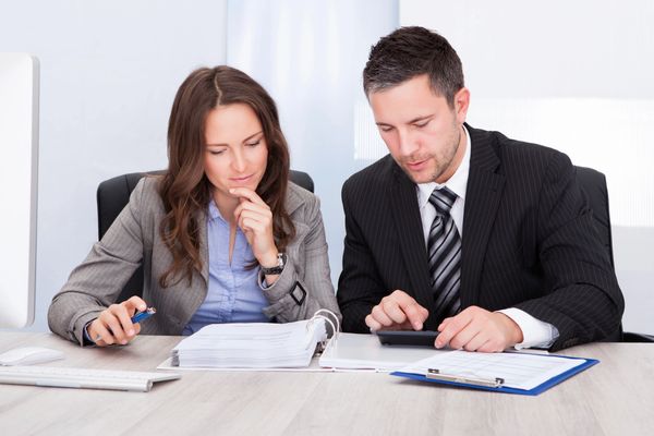 Two professionals reviewing documents with a calculator at the office.