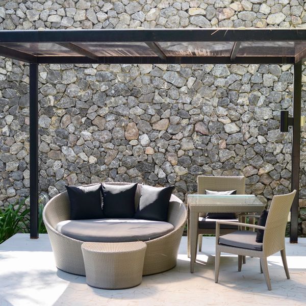 Modern outdoor patio set with stone wall backdrop under a pergola.