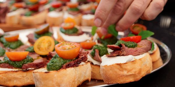 Deli style canapés for a catering event, with cold deli meats, pesto and tomatoes on baguette slices