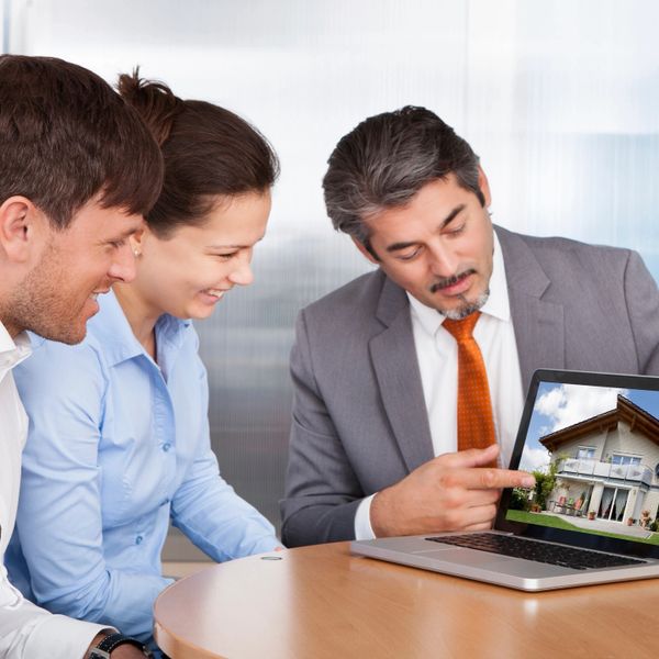 Real estate agent showing a house to a couple on a laptop.