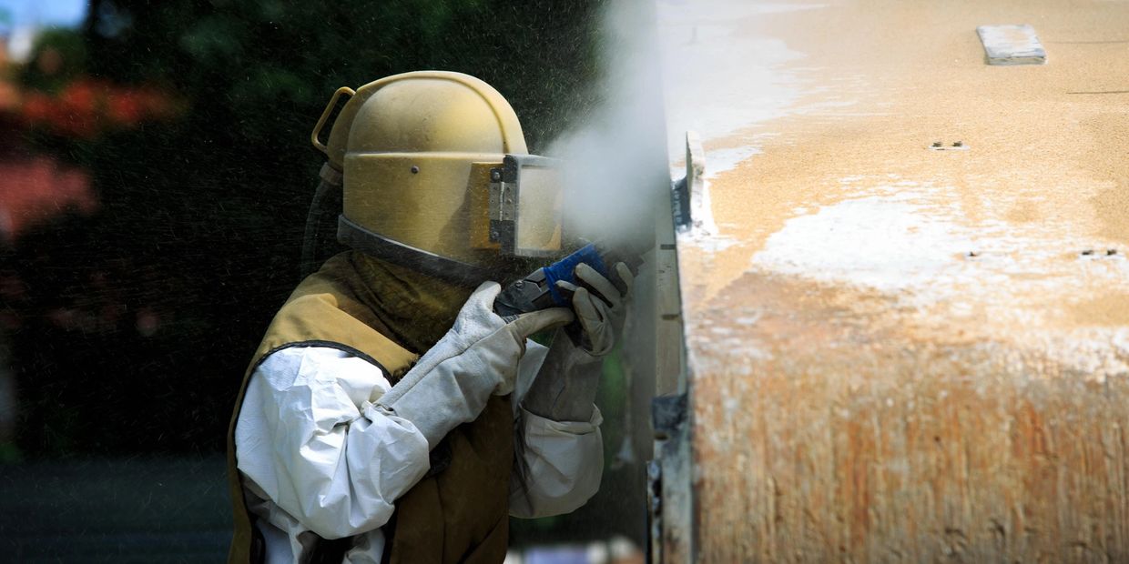 Worker in protective gear sandblasting a surface.