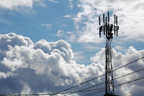 A tall communication tower against a backdrop of fluffy clouds and blue sky.