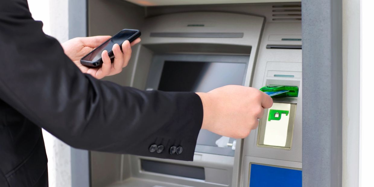 Person inserting a card into an ATM while holding a smartphone.