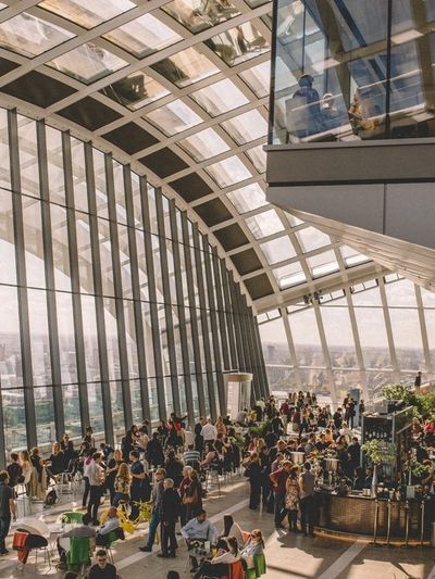 A large indoor space with curved glass walls filled with people and plants.