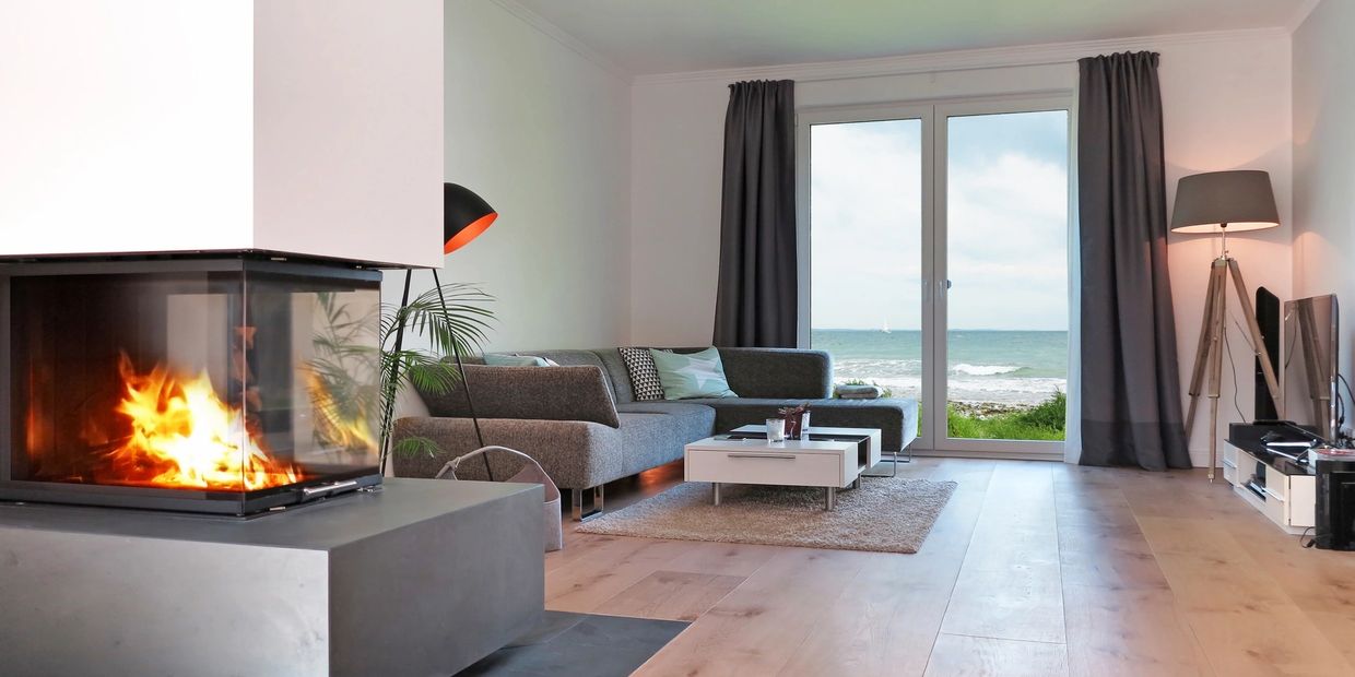 Modern living room with fireplace and ocean view through large glass doors.