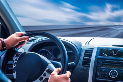 Person driving a car on a blurred road with hands on the steering wheel.