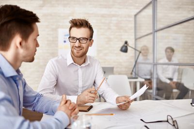 Two men discussing holding pen and paper