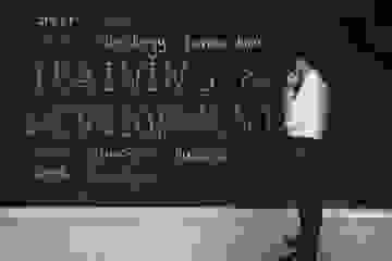 A businessman standing in front of a blackboard wall with words written in chalk on it.