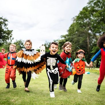 Children joyfully running outdoors in colorful Halloween costumes.