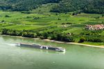 Cargo ship sailing on a river beside green farmland.