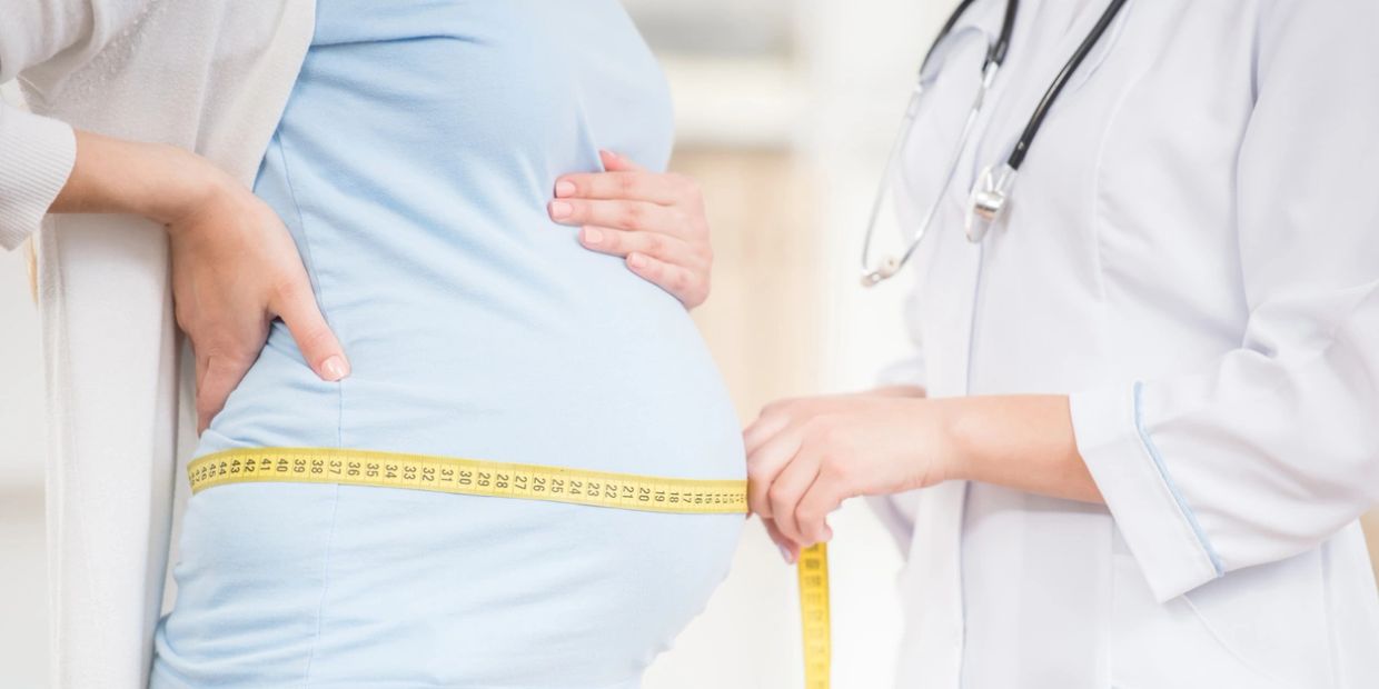 Pregnant woman being measured by a doctor with a tape measure.