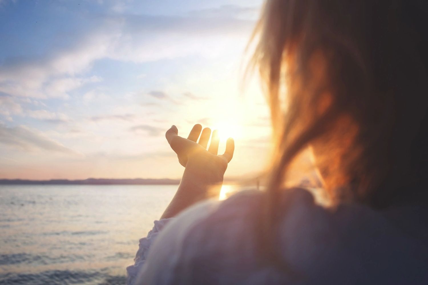 A hand reaching to cradle the sun in front of a lake