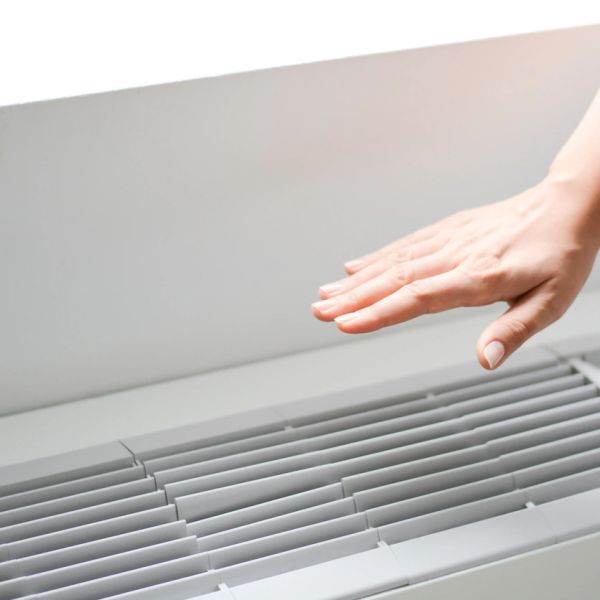 Hand feeling warm air from a heater vent.