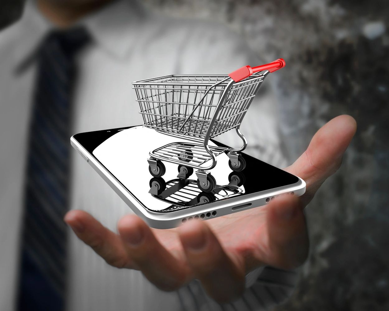 Mini shopping cart on a smartphone held by a person in a suit.