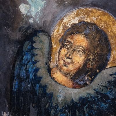 Ancient fresco of an angel with a golden halo and blue wings.