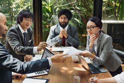 CEO wearing turban, consulting with virtual CIO and IT team around conference table with laptops.