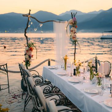Elegant outdoor dining setup by the water during sunset with floral decorations.