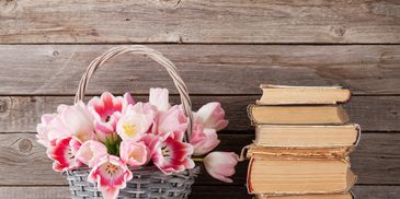 Flowers placed in a basket next to a stack of old books. 