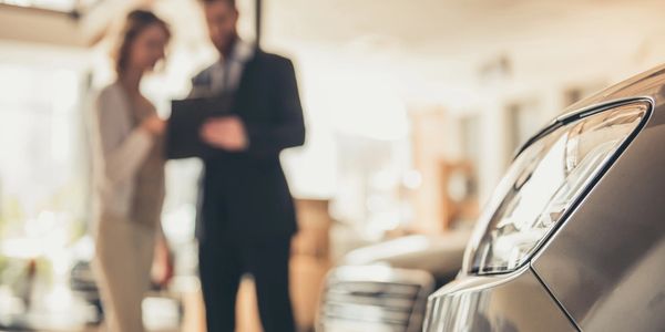 Two people discussing near a car in a showroom.