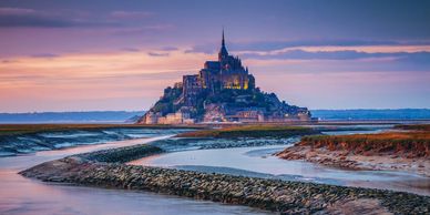 Mont Saint-Michel illuminated at dusk with winding tidal waters.