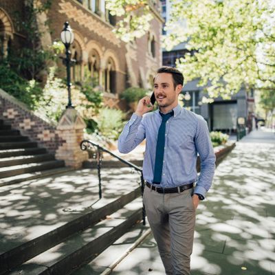 Man walking outdoors, talking on a phone, dressed in business casual attire.