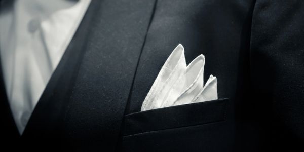 Close-up of a white pocket square in a black suit jacket pocket.