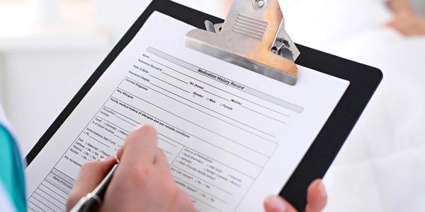 Person filling out a medication history record on a clipboard.