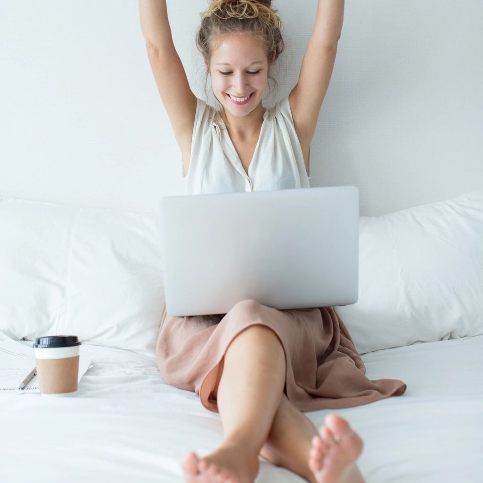 A happy women in white clothes looking at her laptop with a coffee mug