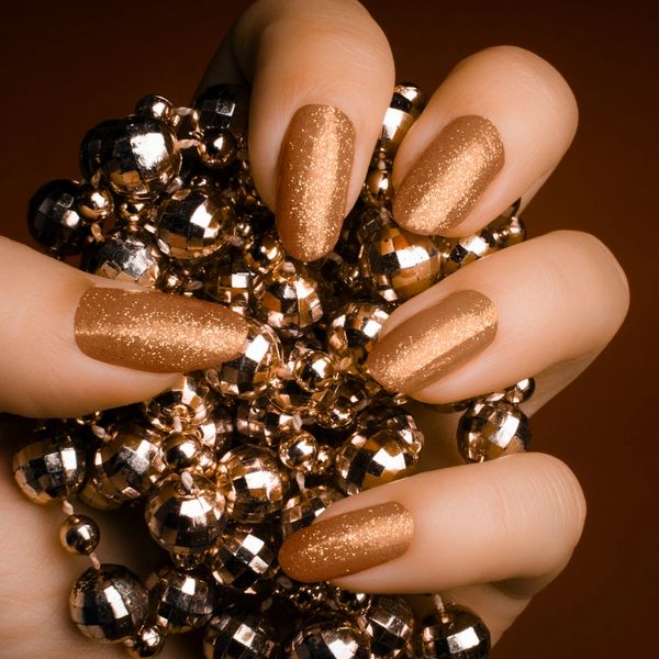 Hand with glittery golden nails holding shiny golden beads.
