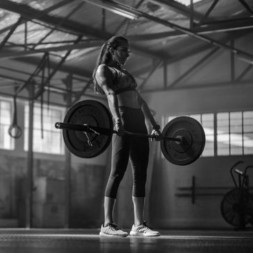 Woman lifting a barbell in a crossfit or hyrox gym with natural light.