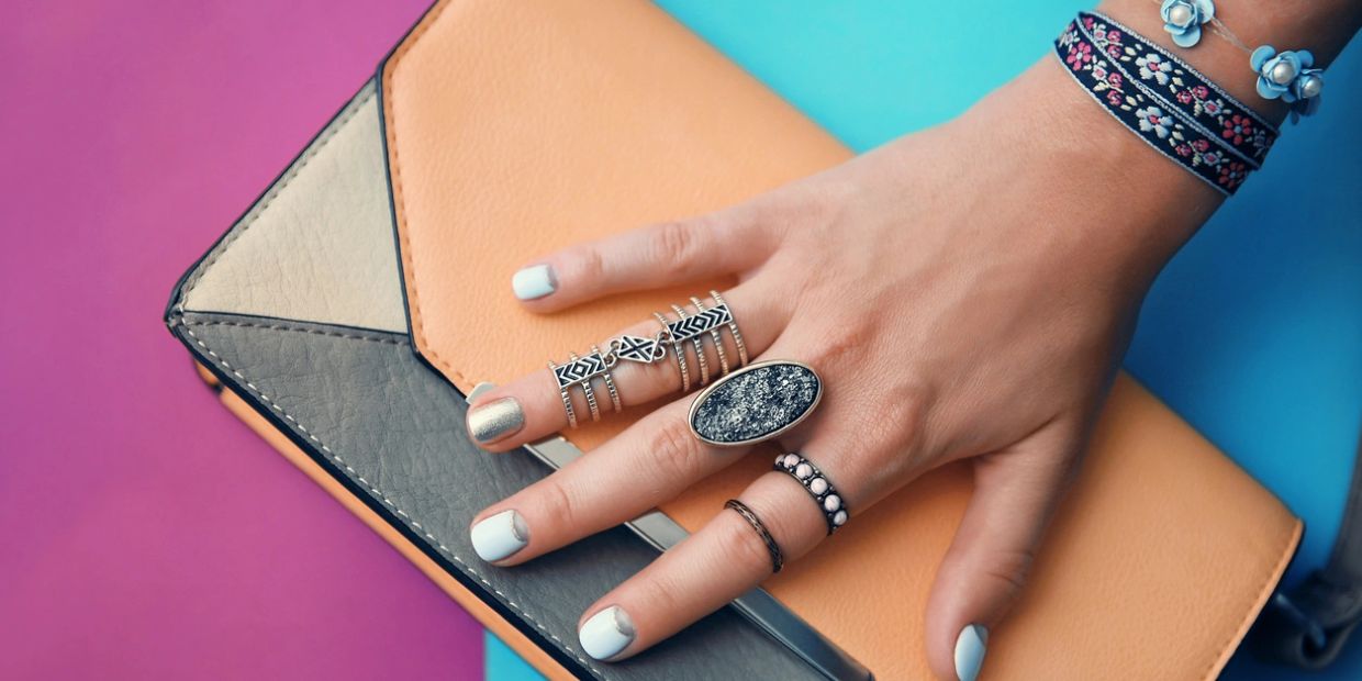 Hand adorned with rings and bracelets resting on a color-blocked purse.