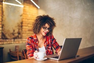 eager young woman seated at open notebook computer with coffee in hand