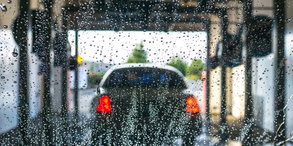 View through a rain-covered car windshield at a vehicle ahead in a tunnel.